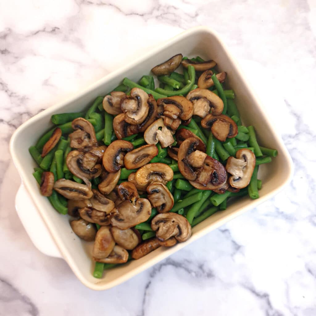 Blanced green beans and browned mushrooms in a casserole dish.
