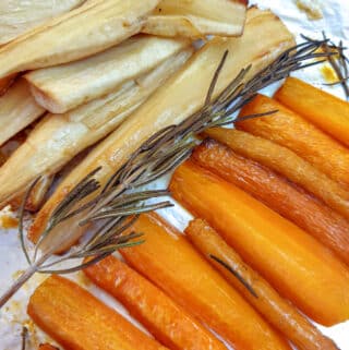 Honey-roasted carrots and parsnips on a baking tray with a sprig of rosemary.