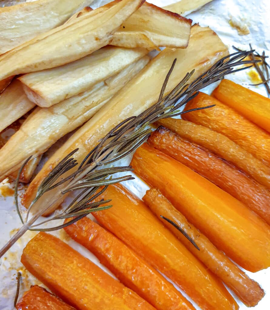 Honey-roasted carrots and parsnips on a baking tray with a sprig of rosemary.