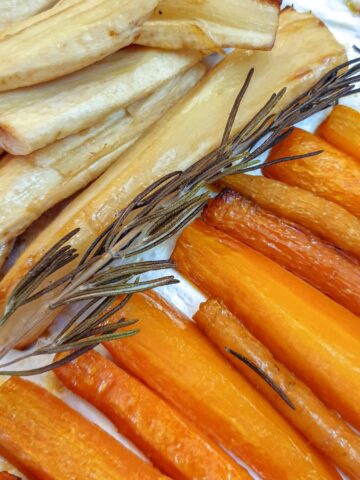 Honey-roasted carrots and parsnips on a baking tray with a sprig of rosemary.