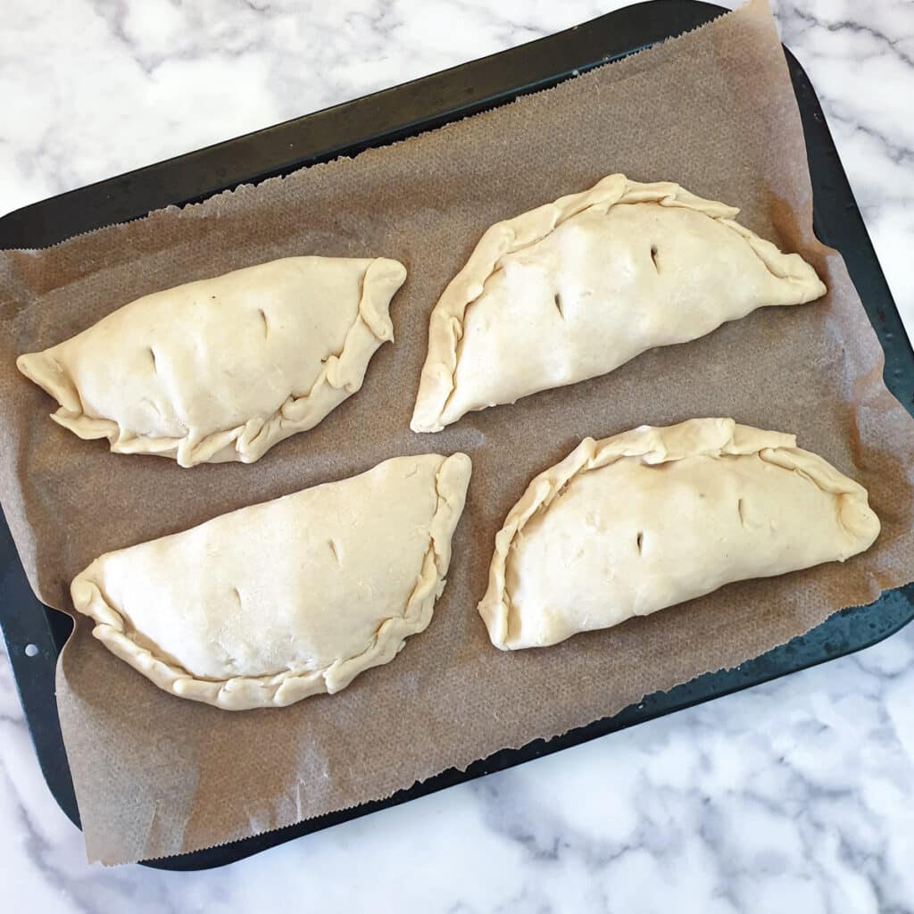 4 formed Cornish pasties on a baking sheet.