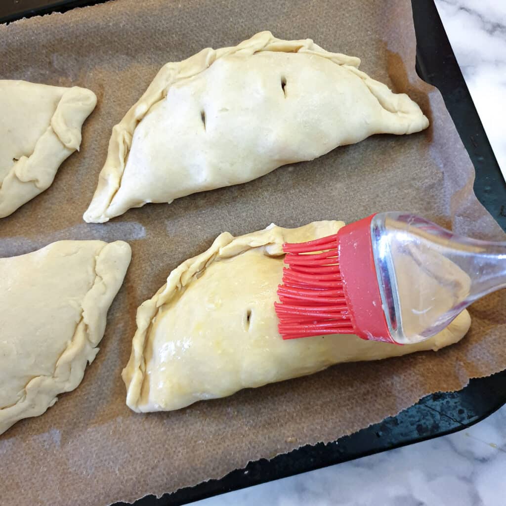 Cornish pasties being brushed with beaten egg.