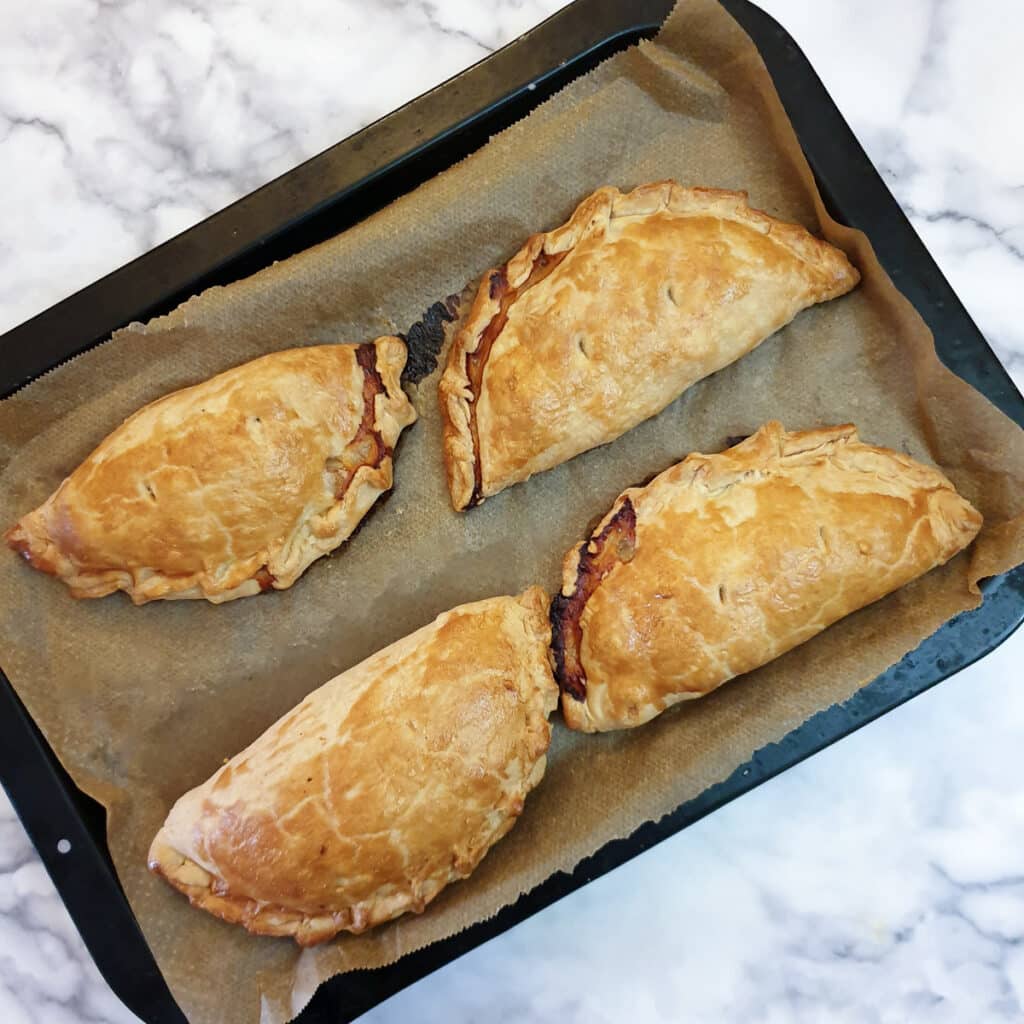 4 baked Cornish pasties on a baking sheet.