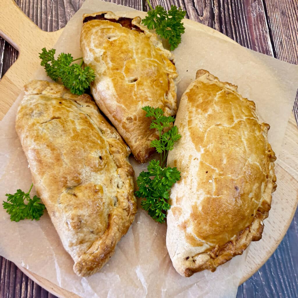 Three Cornish pasties on a wooden board.