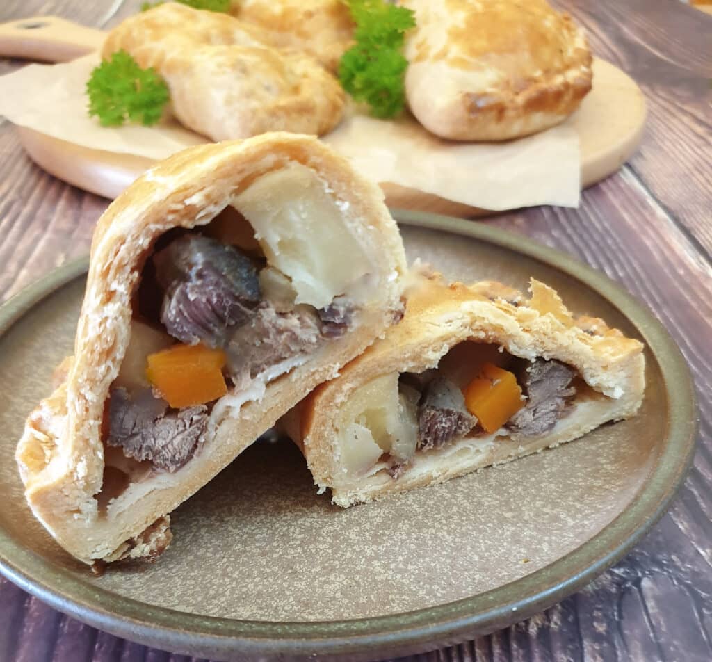 A Cornish pasty on a brown plate, cut open to show the inside.