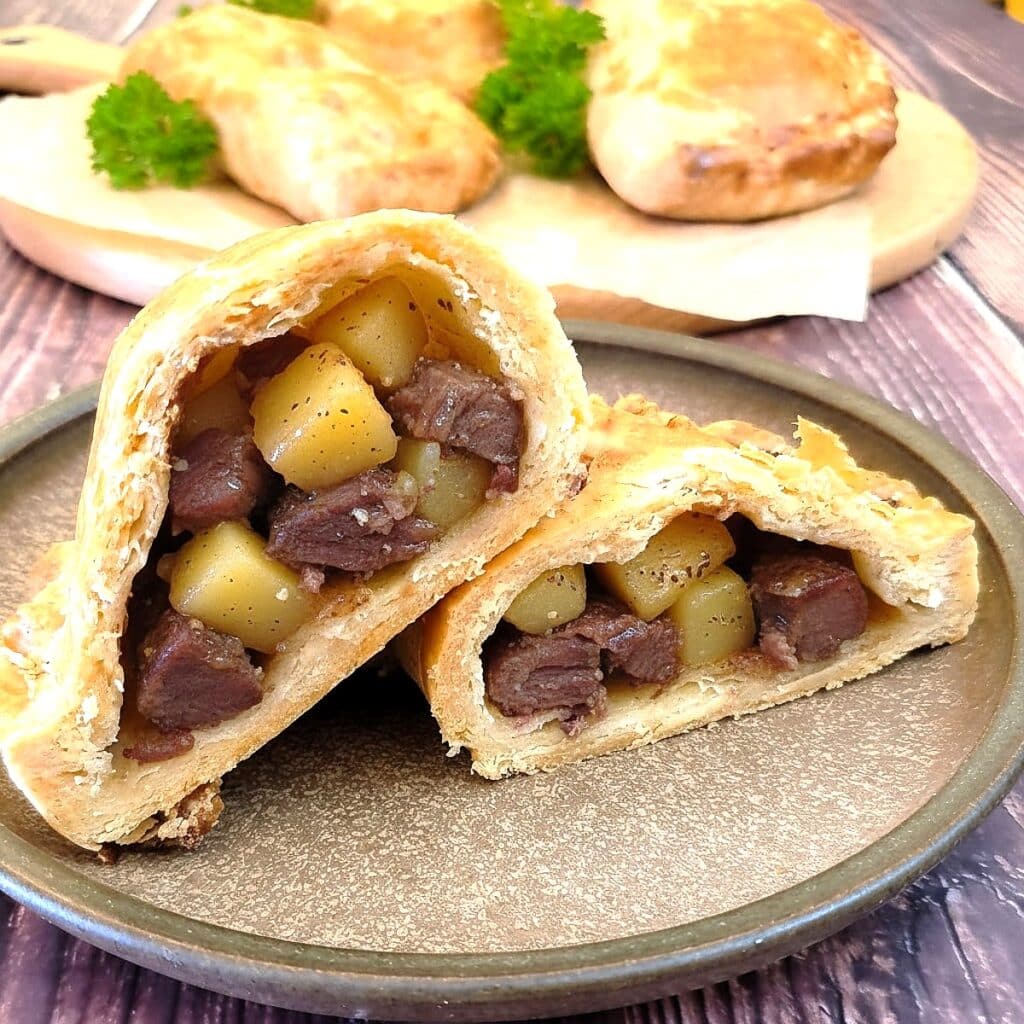 A Cornish pasty, cut in half to show the inside, on a brown plate,.