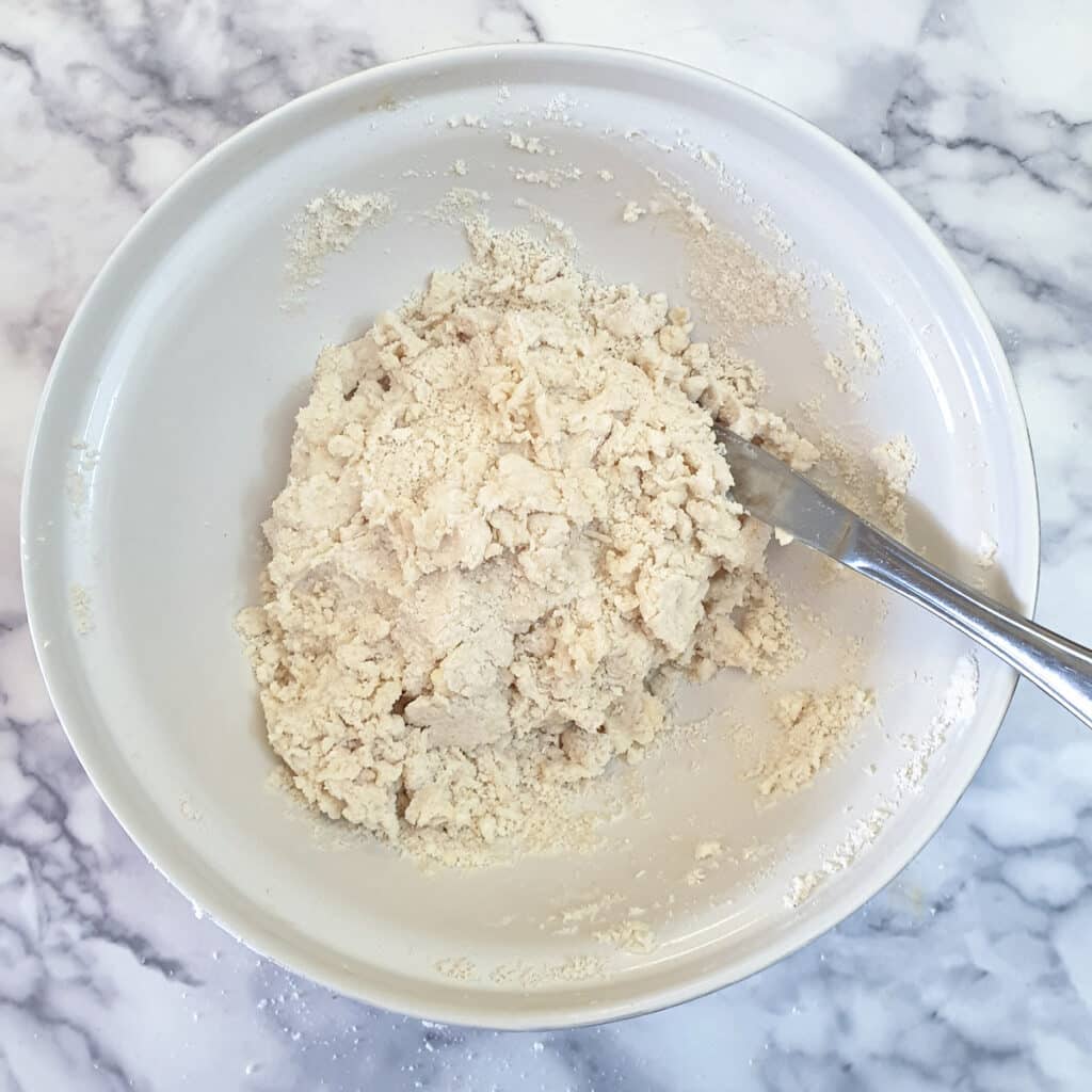 A mixing bowl containing flour and butter, mixed with water to form a shaggy dough.