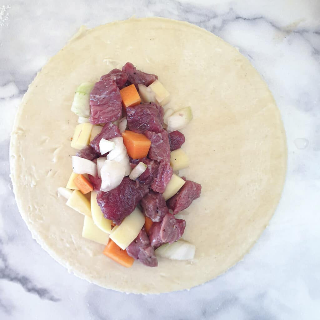 A circle of dough topped with a large spoonful of meat and vegetable filling.