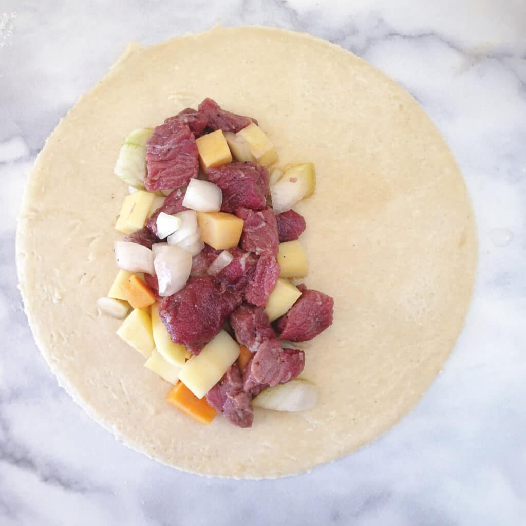 A circle of dough topped with a large spoonful of meat and vegetable filling.