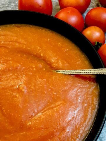 Tomato passata in a black serving dish next to a pile of fresh tomatoes.