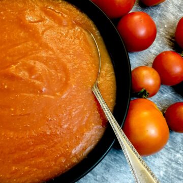 Tomato passata in a black serving dish next to a pile of fresh tomatoes.