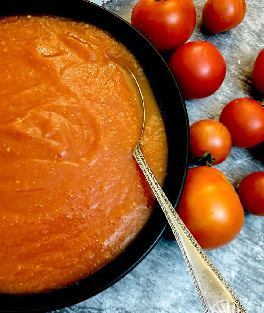 Tomato passata in a black serving dish next to a pile of fresh tomatoes.