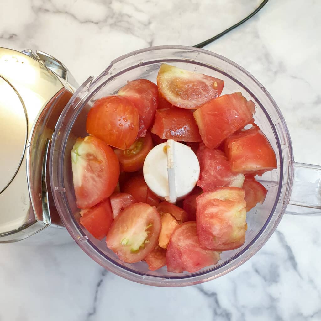 Quartered tomatoes in a food processor.