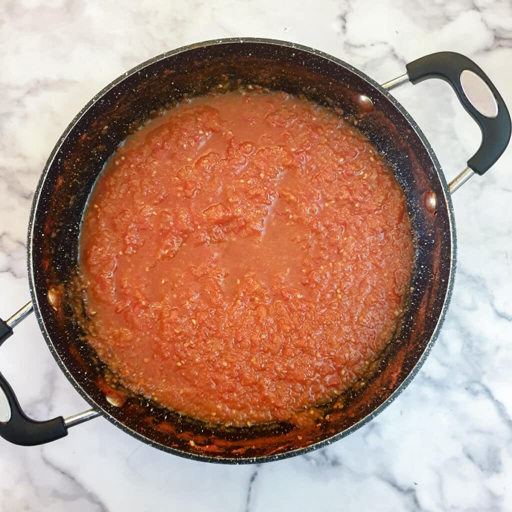 A large frying pan containing watery passata.