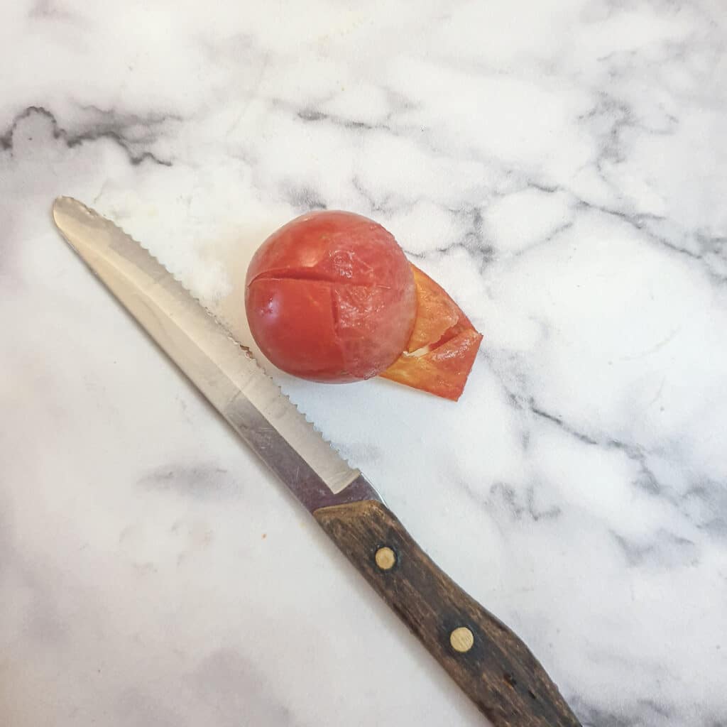 A tomato with a knife showing the skin being peeled away.