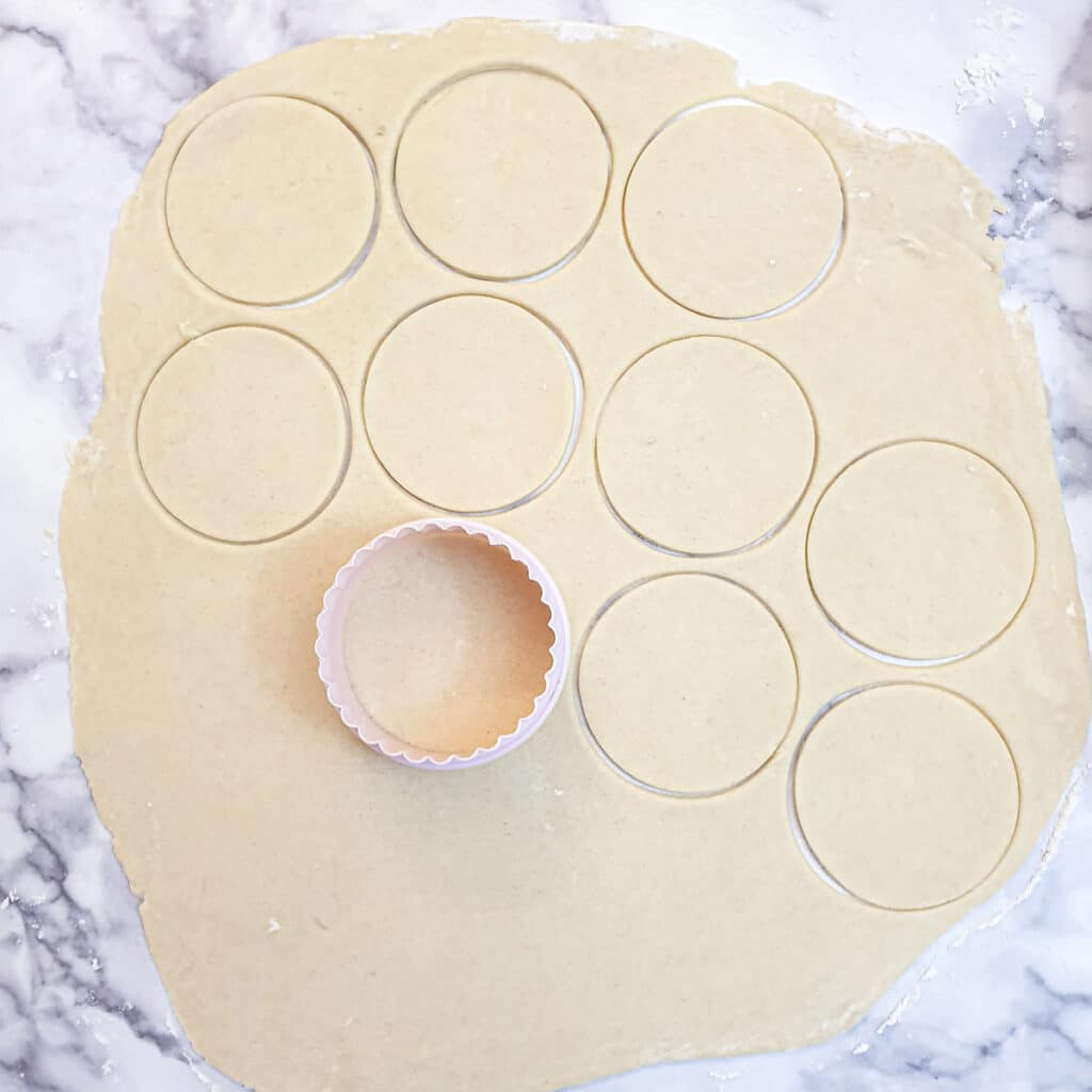 Thinly rolled pastry being cut into small circles with a round  pastry cutter.