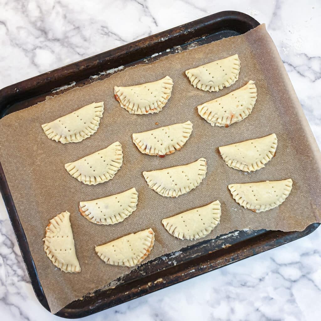 13 jam turnovers on a baking sheet.