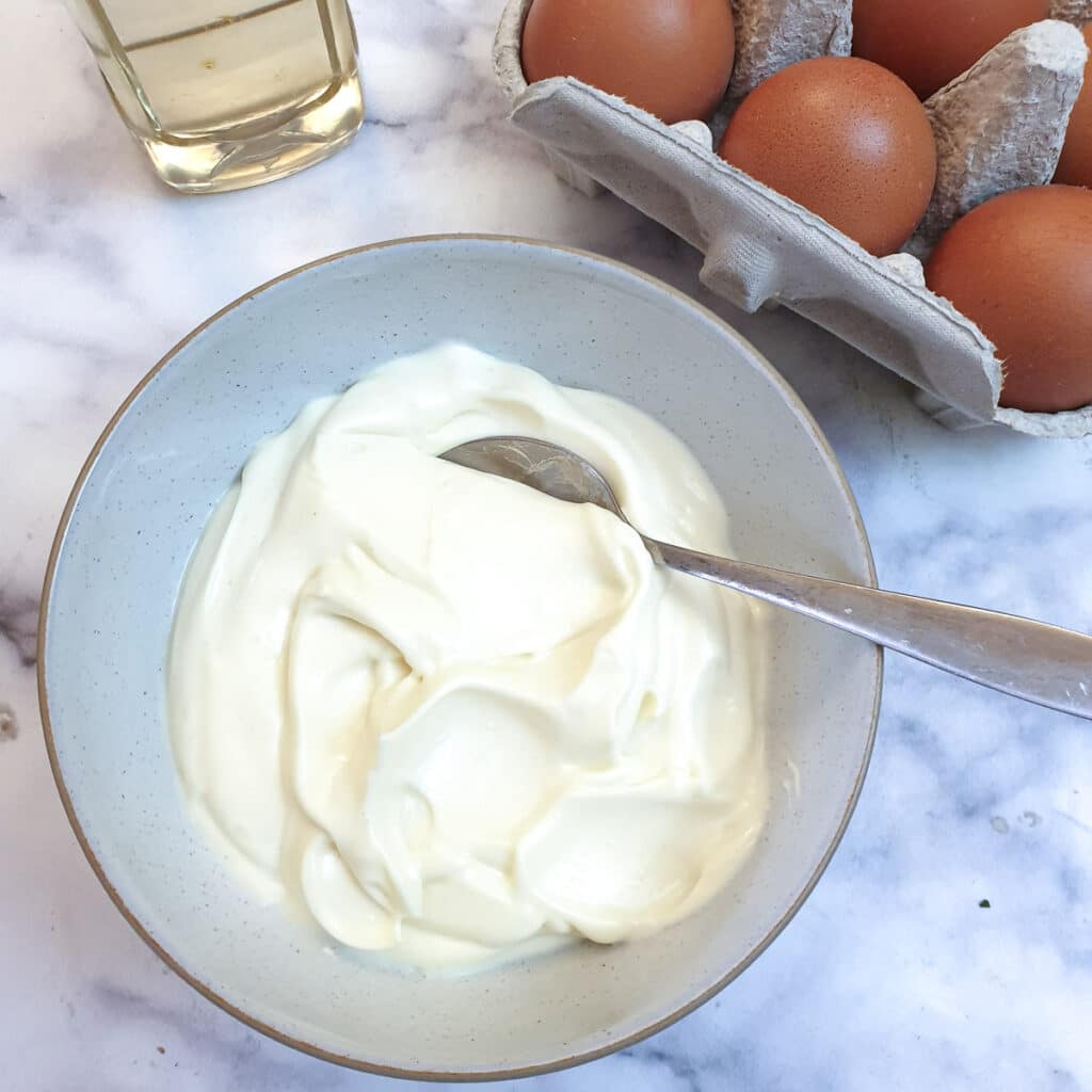 A bowl of one-minute mayonnaise with a spoon next to a box of eggs.