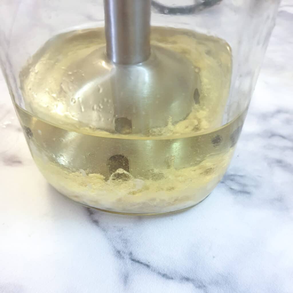 Close up of a stick blender mixing egg and oil in a bottle.