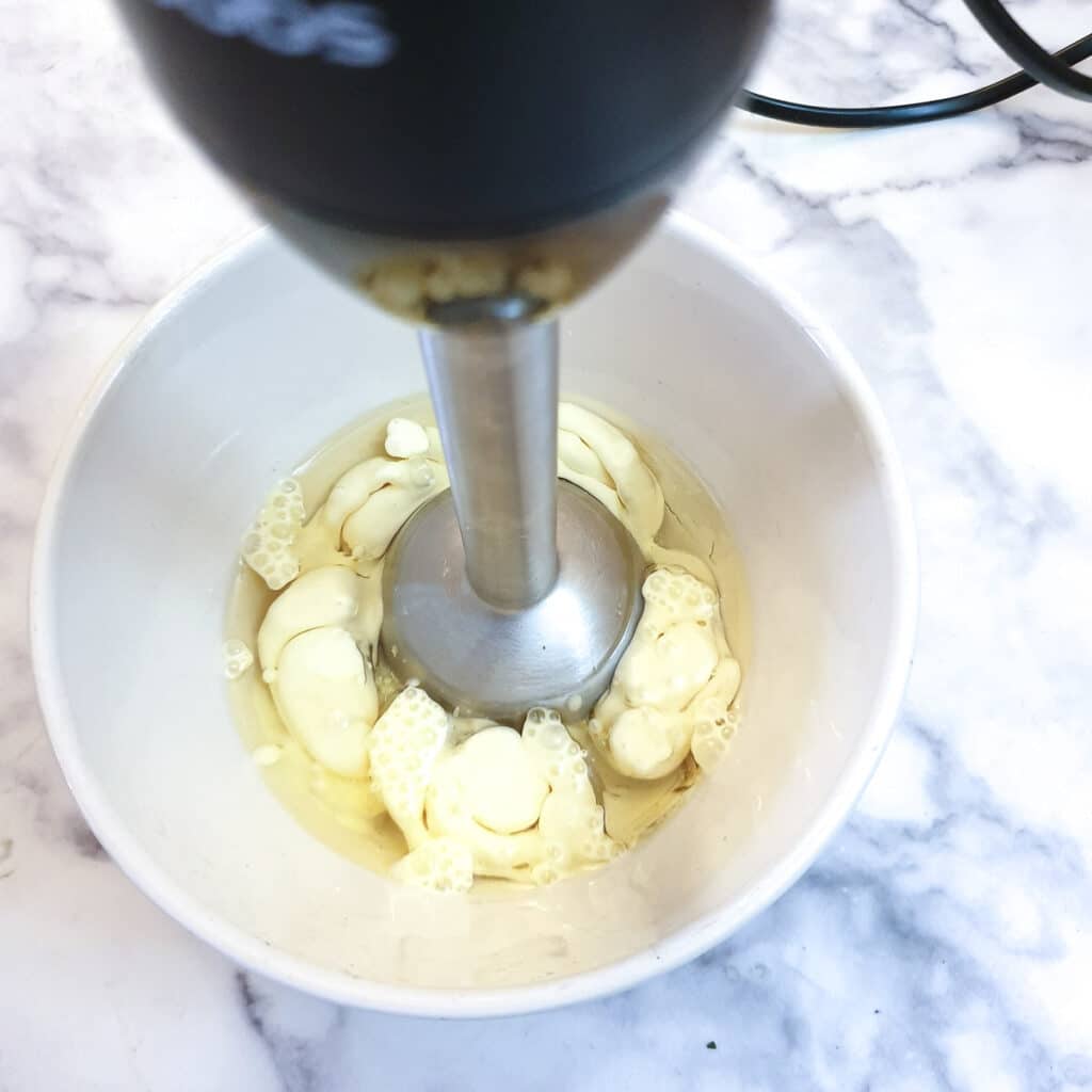 Egg and oil starting to emulsify as they are being blended in a bowl.