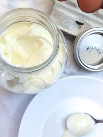 A jar of mayonnaise behind a spoonful of mayonnaise on a white plate.