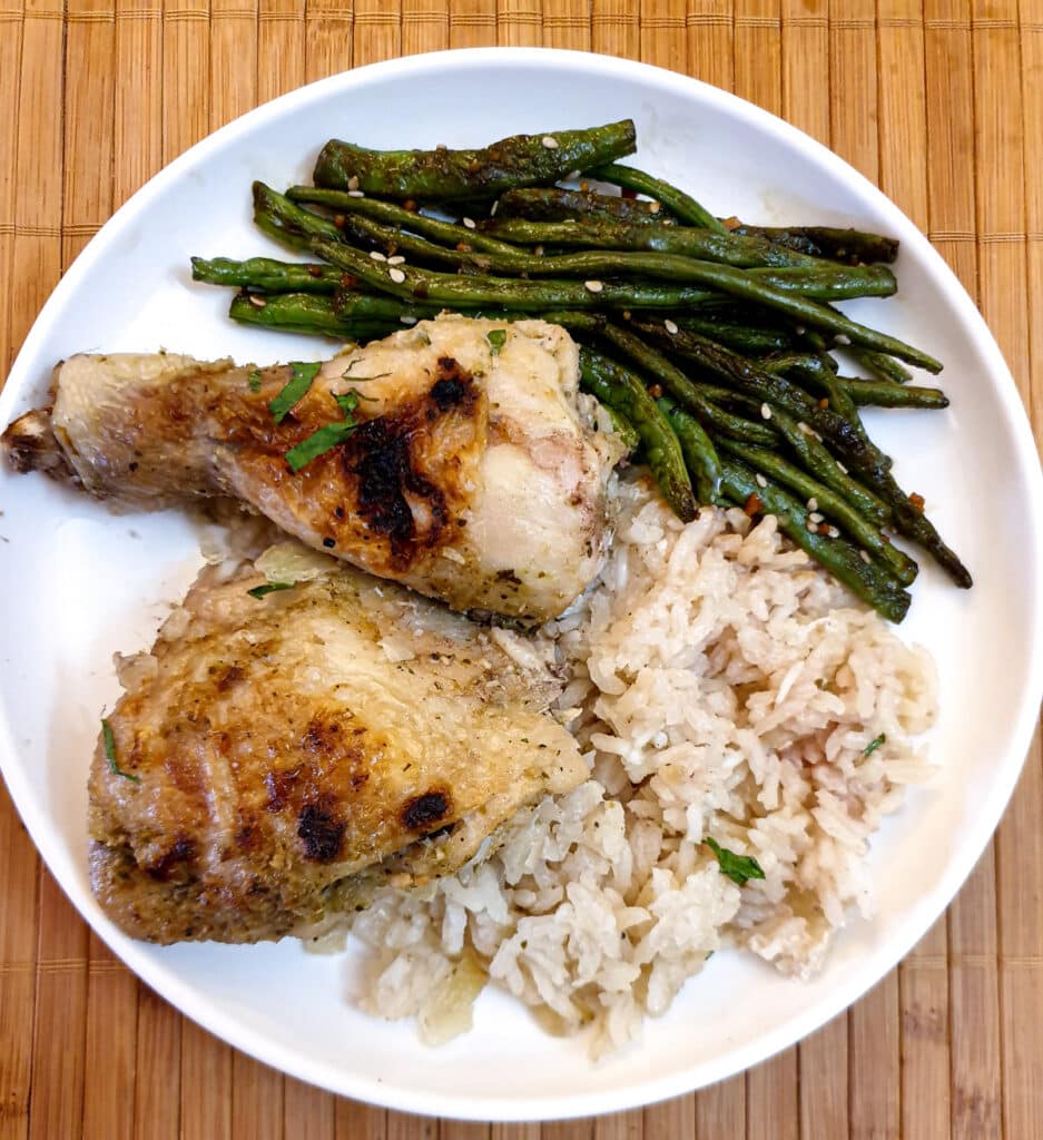 2 pieces of chicken on a white plate with rice and Chinese green beans.