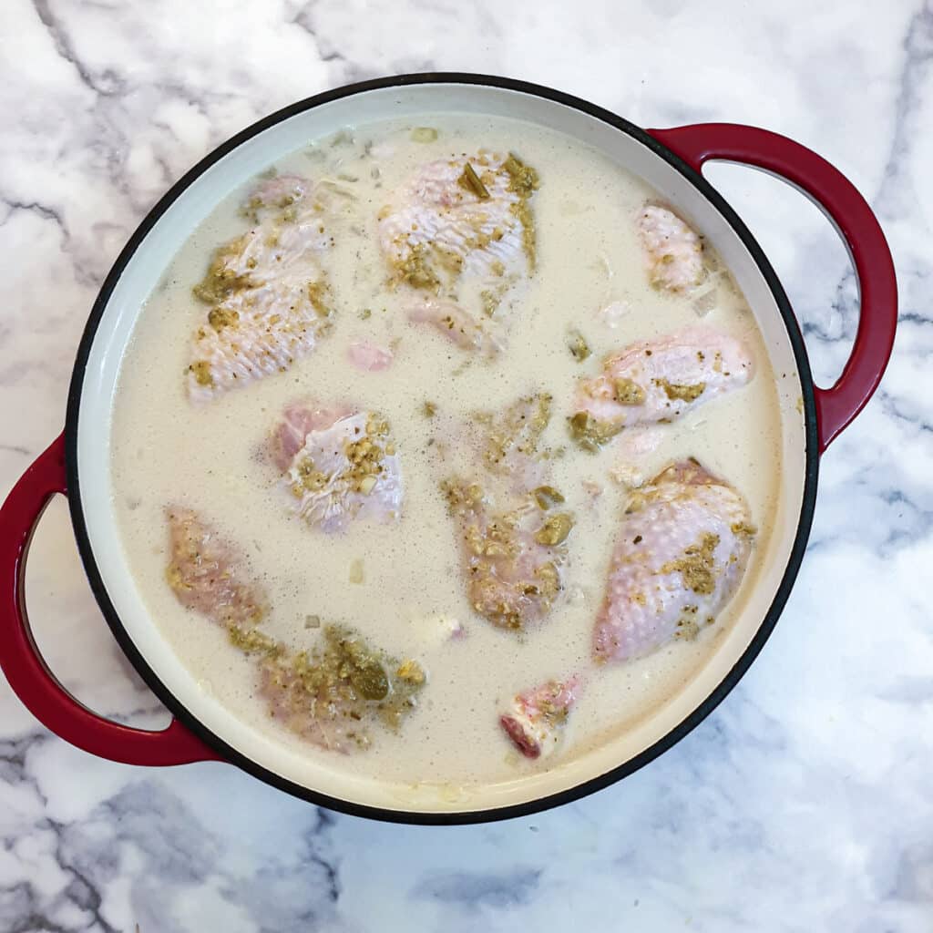 Marinated chicken pieces added to stock in a large pan.