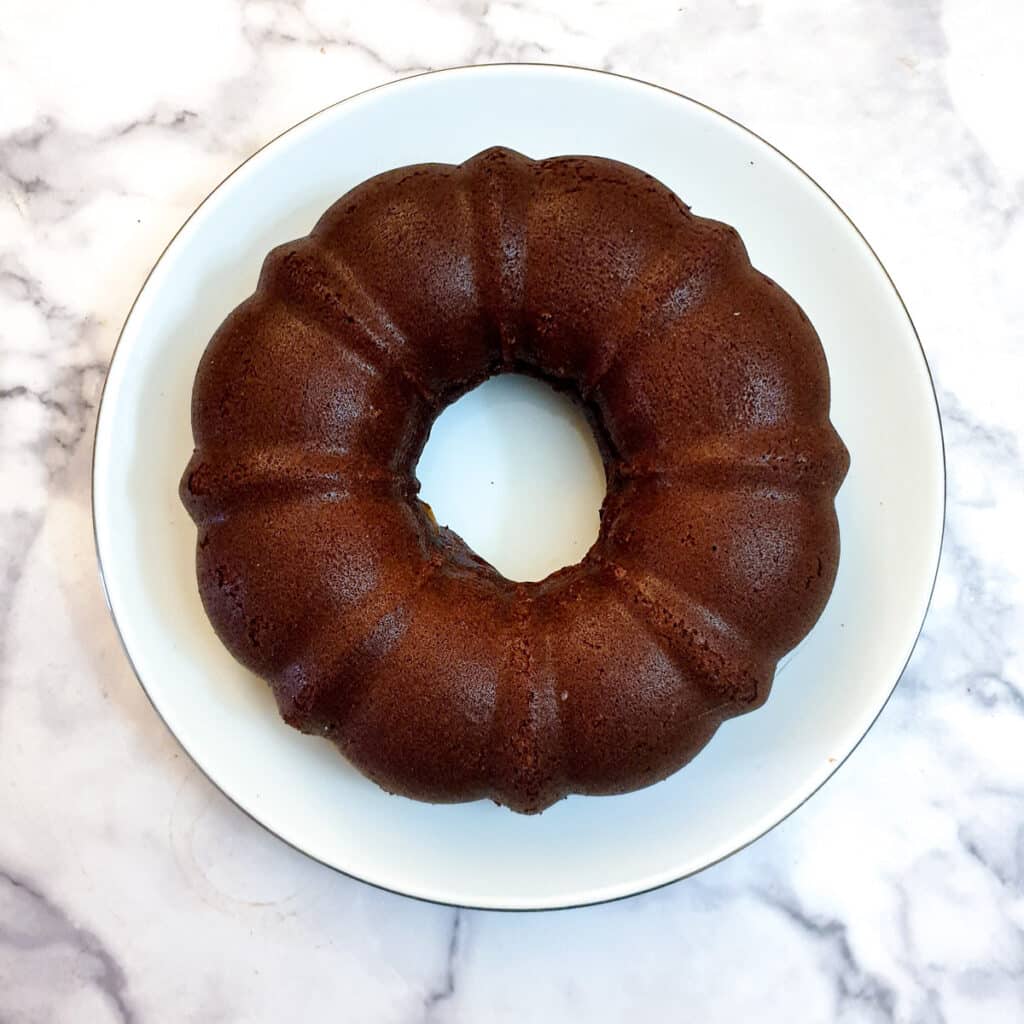 A round chocolate cake tipped out of the bundt pan onto a white plate.