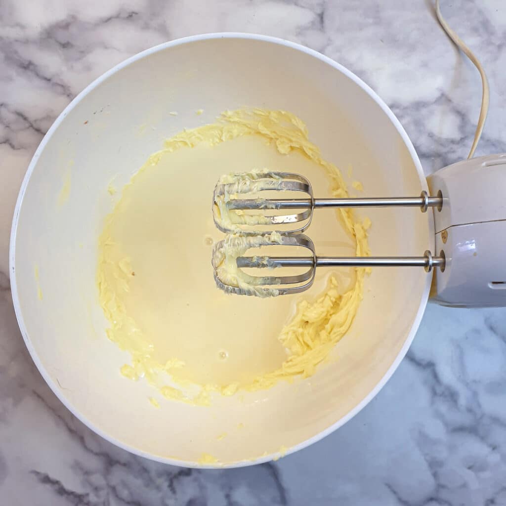 Condensed milk poured into beaten butter in a white bowl.