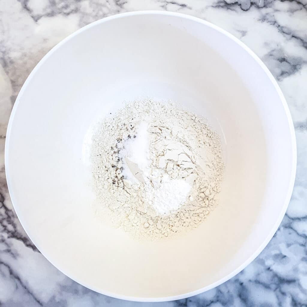 Flour, baking powder, salt and pepper in a white mixing bowl.