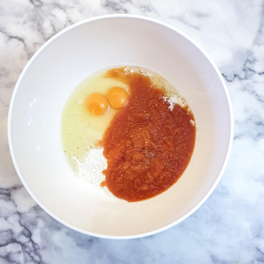 Eggs and passata with flour in a white mixing bowl.