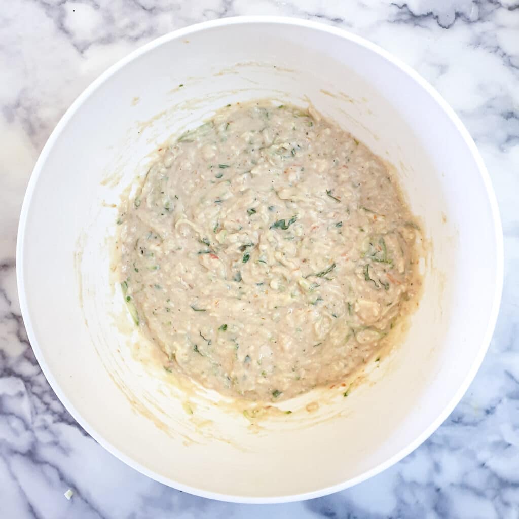 A white mixing bowl containing the mixed batter for courgette and tomato puffs.