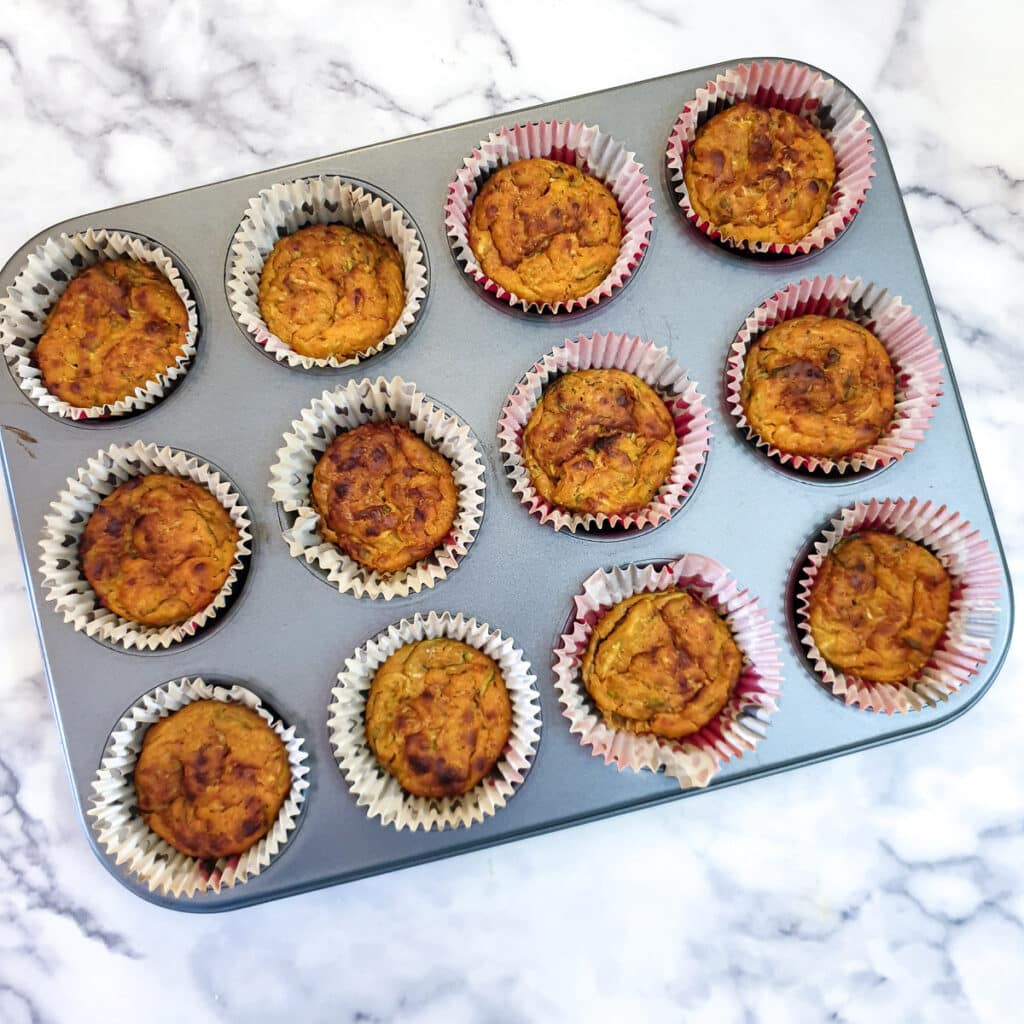 12 baked courgette and tomato puffs in baking cases in a 12-hole muffin tin.