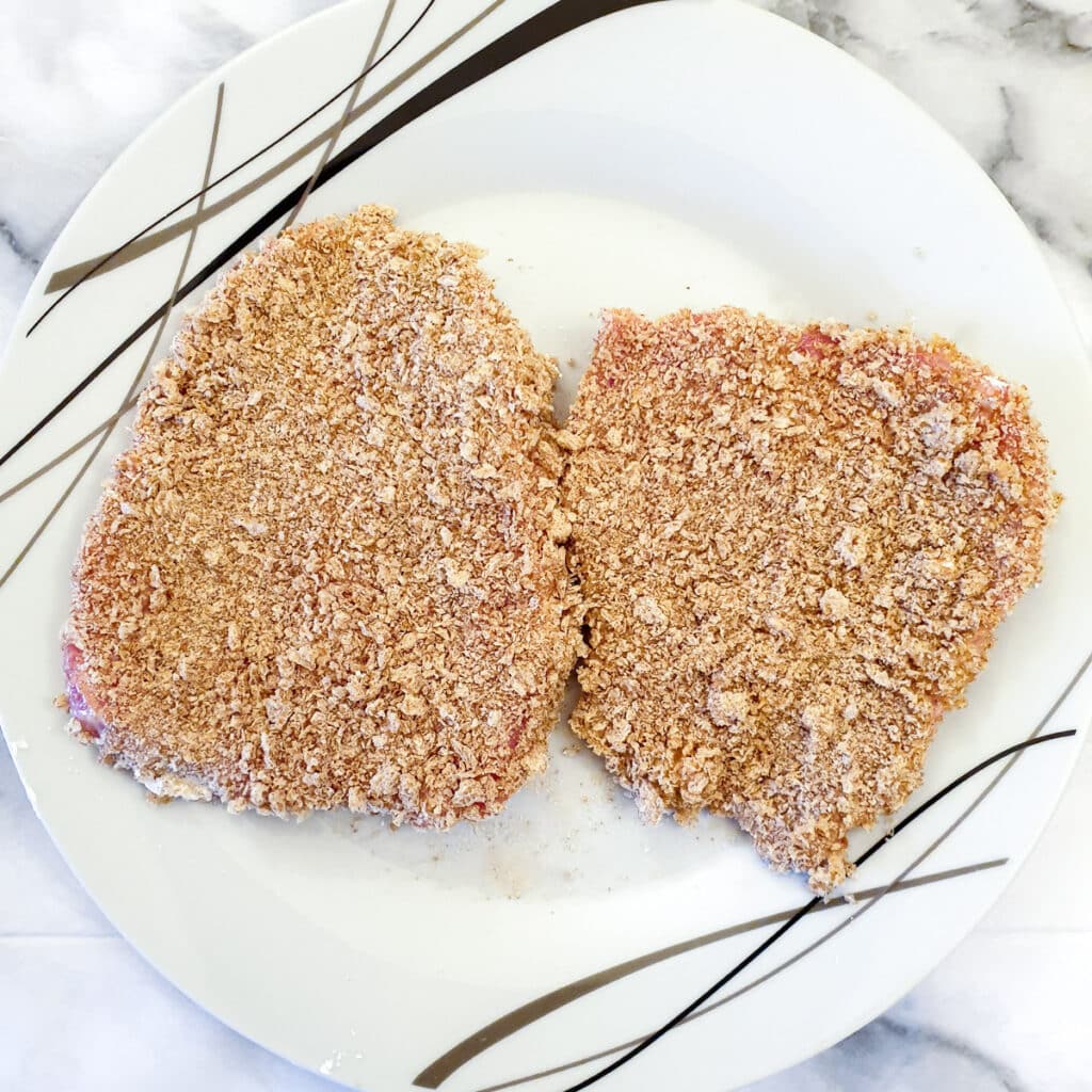 2 coated schnitzels on a plate, ready for frying.