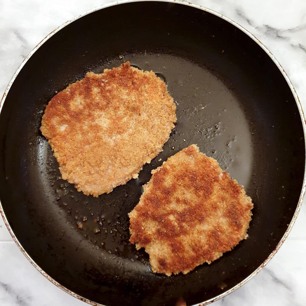 2 schnitzels browning in a frying pan.
