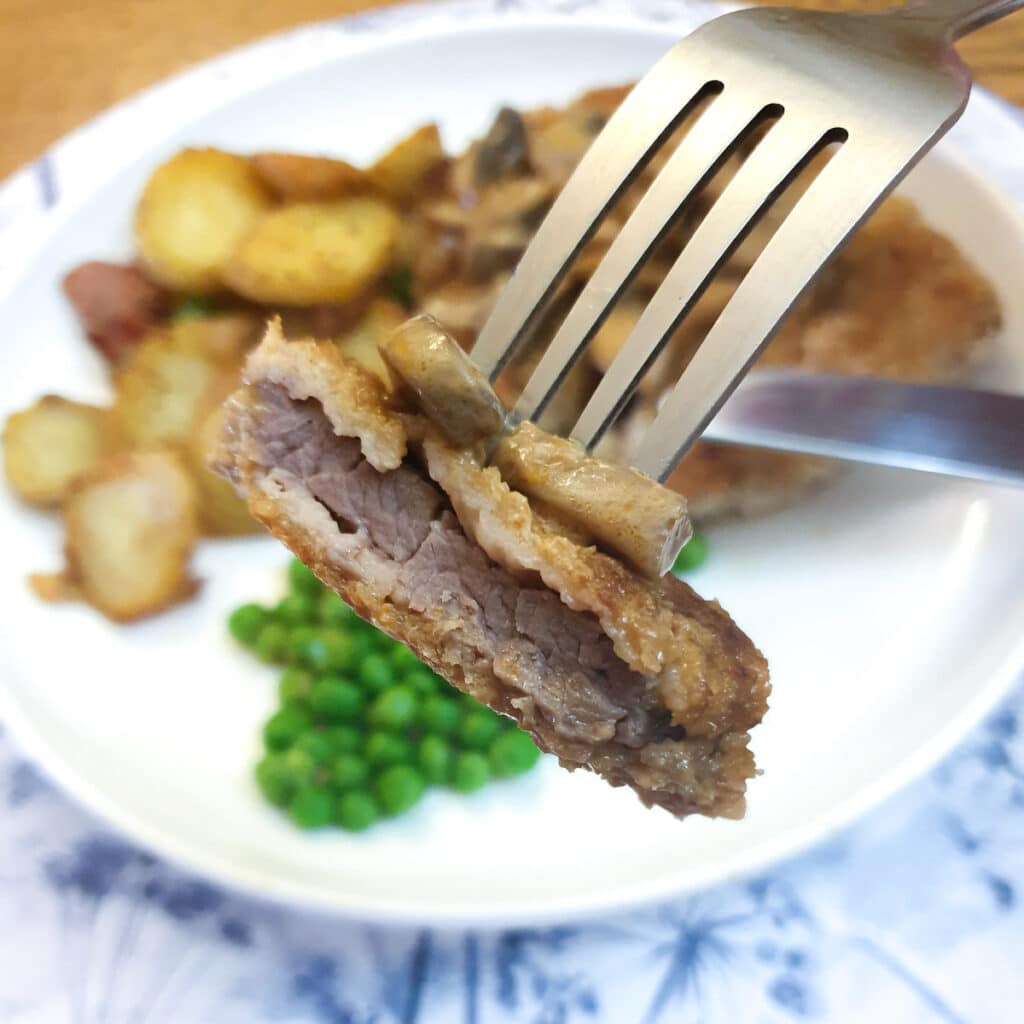 Close up of a piece of crumbed beef schnitzel on a fork.