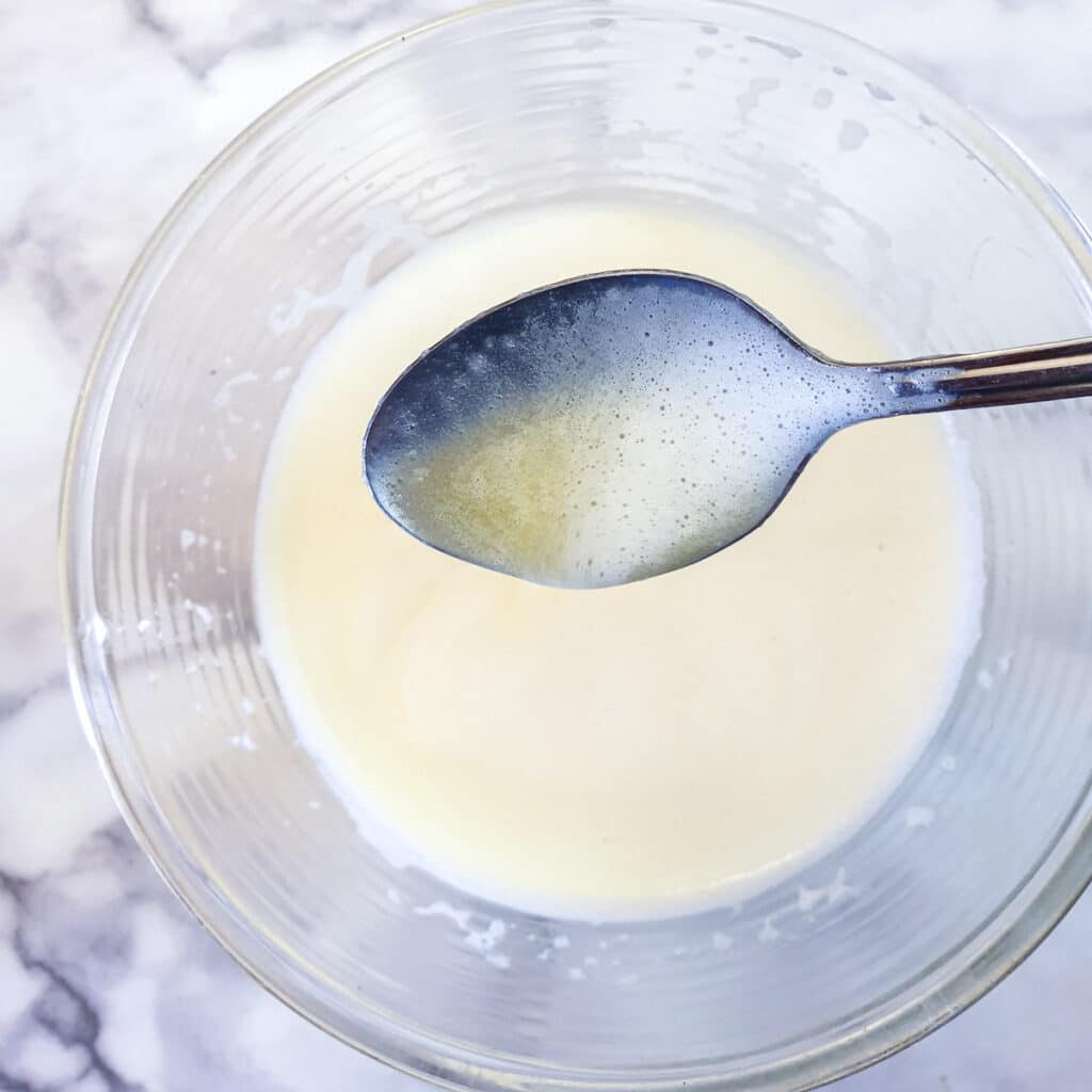 A spoon held over a bowl of eggs, butter and sugar, showing the almost-ready consistency.