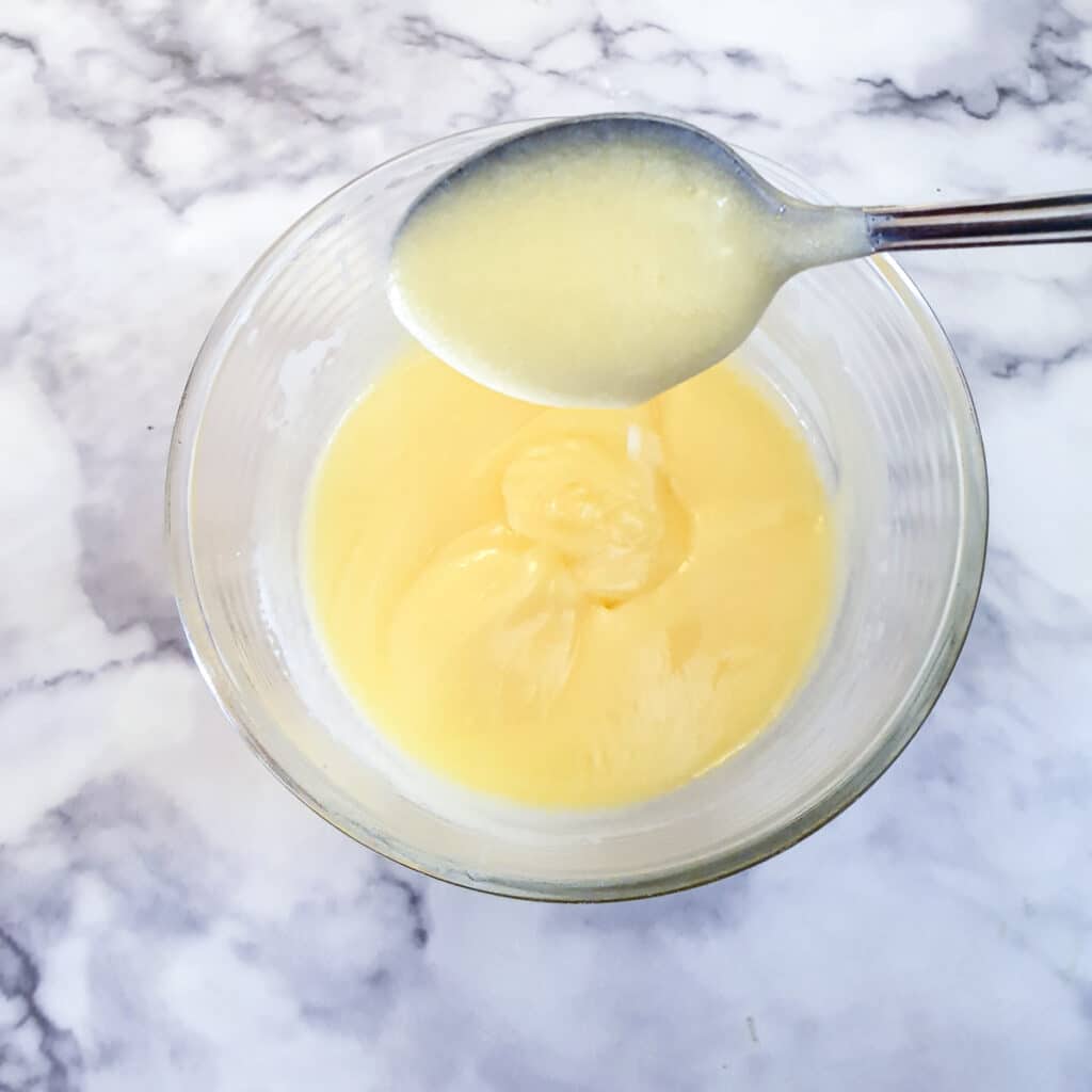 A spoon of thickened lemon curd held over the bowl.