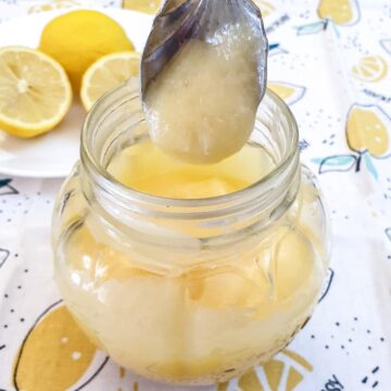 A jar of microwave lemon curd with a spoonful held over the jar.