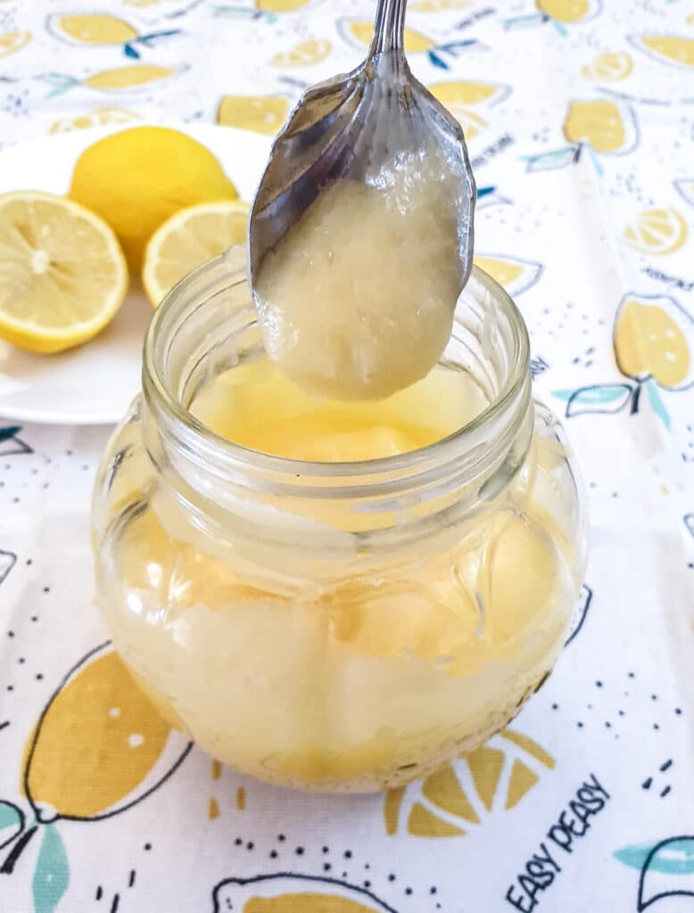 A jar of microwave lemon curd with a spoonful held over the jar.