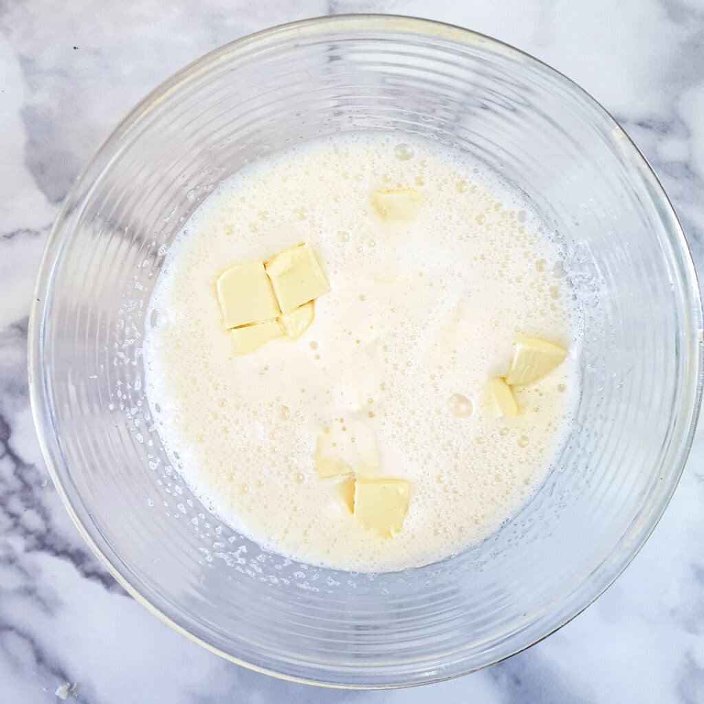 Pieces of butter added to whisked eggs and sugar in a glass bowl.