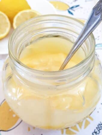 Microwave lemon curd in a glass jar with a spoon.
