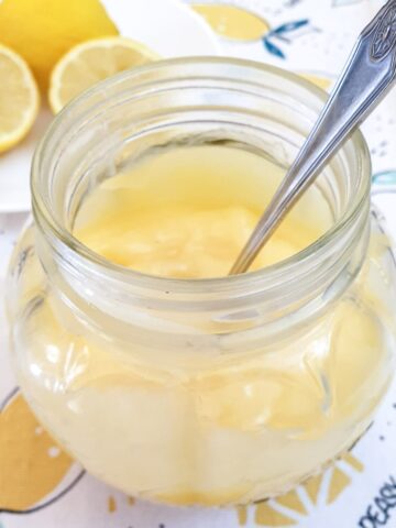 Microwave lemon curd in a glass jar with a spoon.