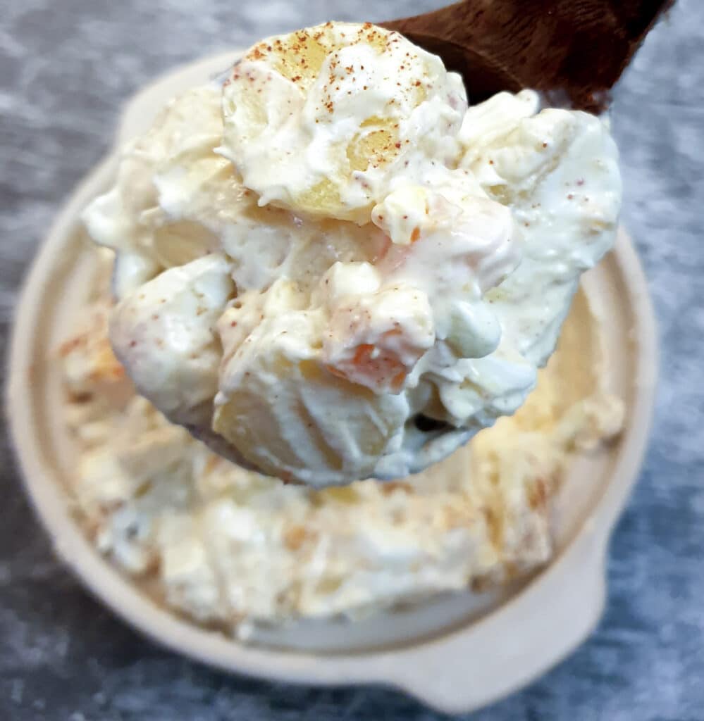 A large spoonful of potato and egg salad held over a serving dish.