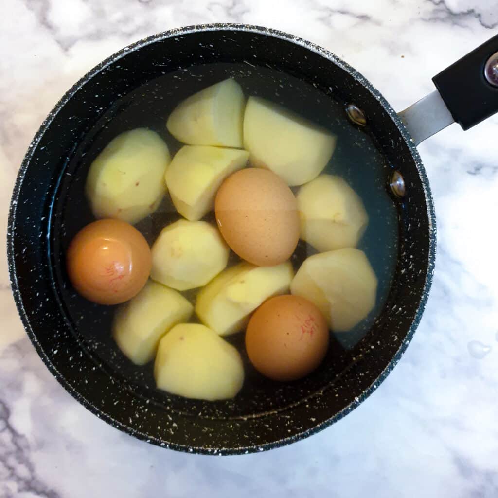 Eggs and large pieces of potato in a saucepan.