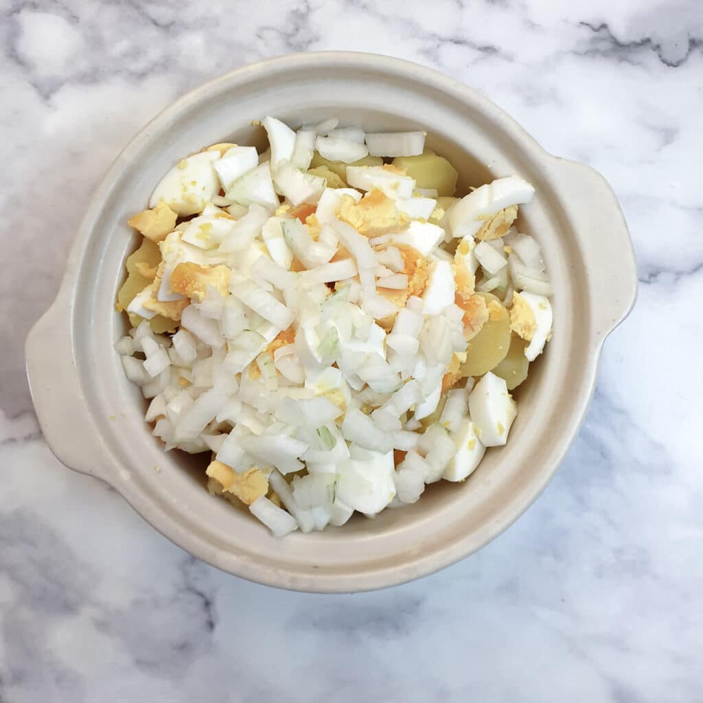 Pieces of cooked potato, hard-boiled egg and chopped onion in a serving dish.