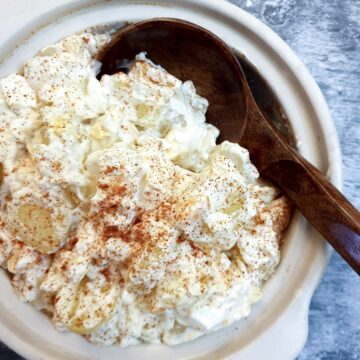 A white serving dish of potato and egg salad with a wooden serving spoon.