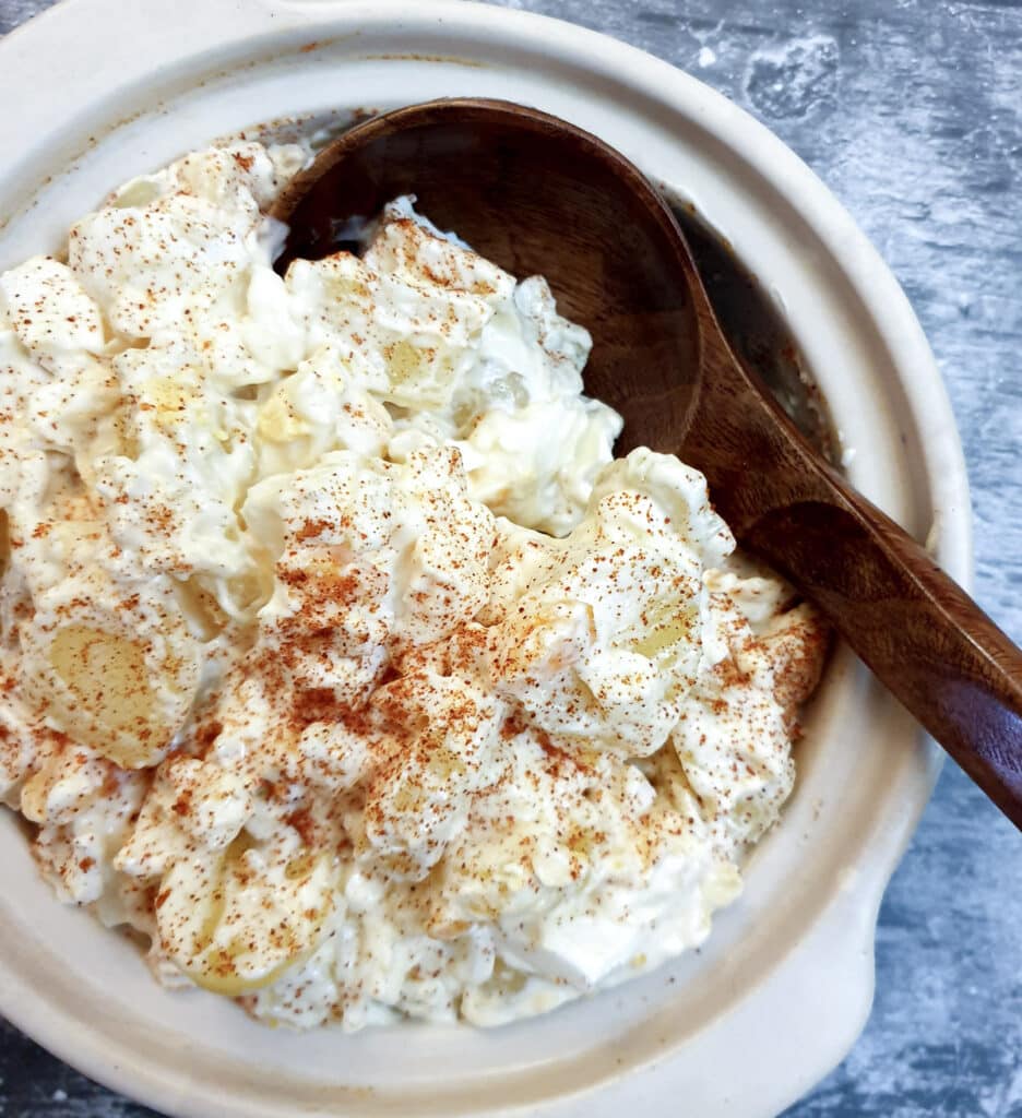 A white serving dish of potato and egg salad with a wooden serving spoon.