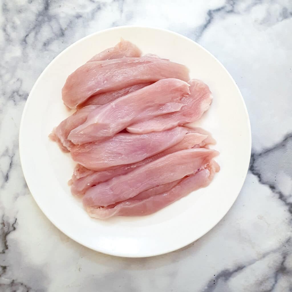 Strips of chicken breast on a white plate.