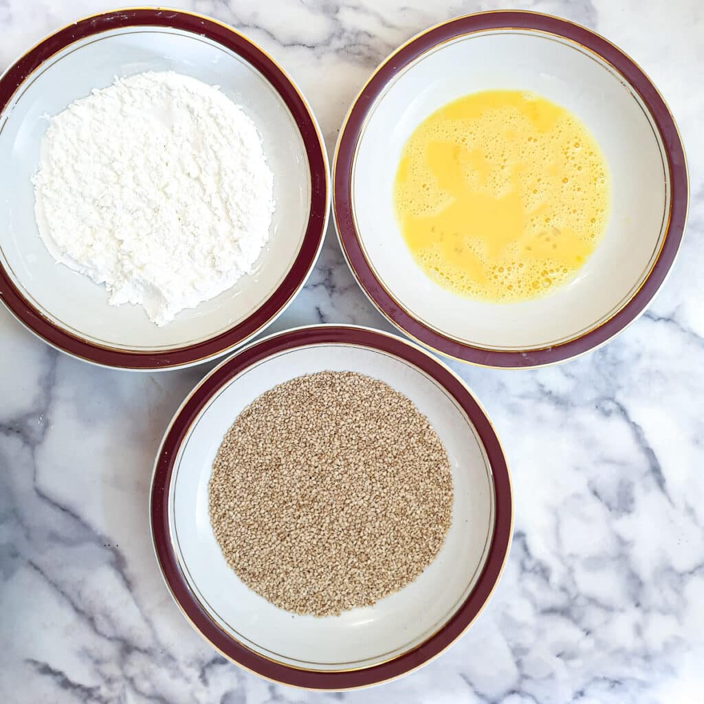 Three bowls with cornflour in the one, beaten in in another and sesame seeds in a third.